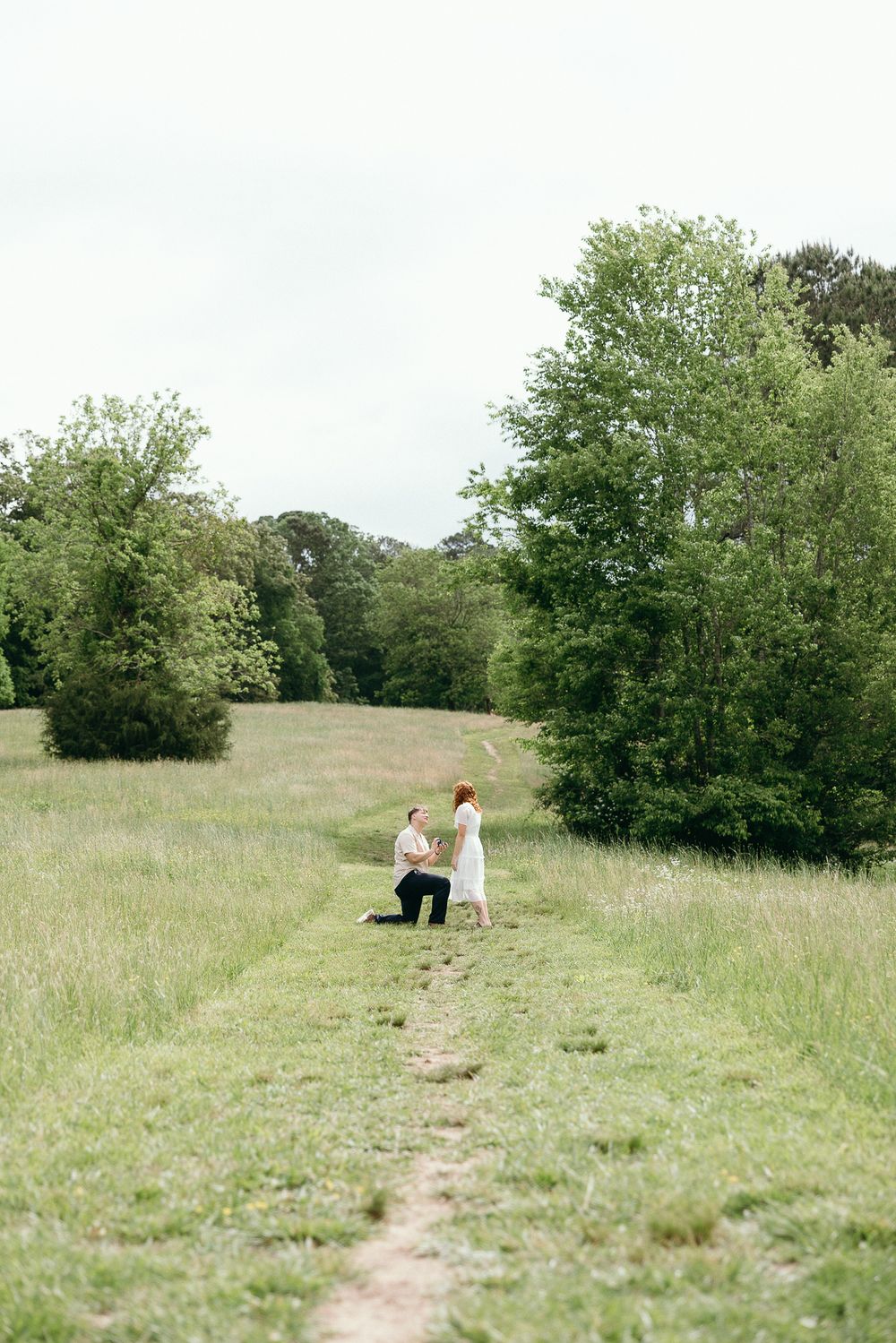 Two figures walk along a winding dirt path through a sunny meadow landscape. Le Château du Cœur Wedding Photographer