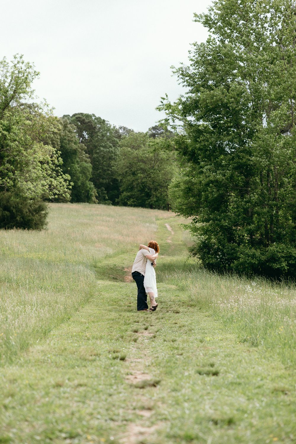 A couple shares a special moment on a grassy hillside path surrounded by nature. Le Château du Cœur Wedding Photographer