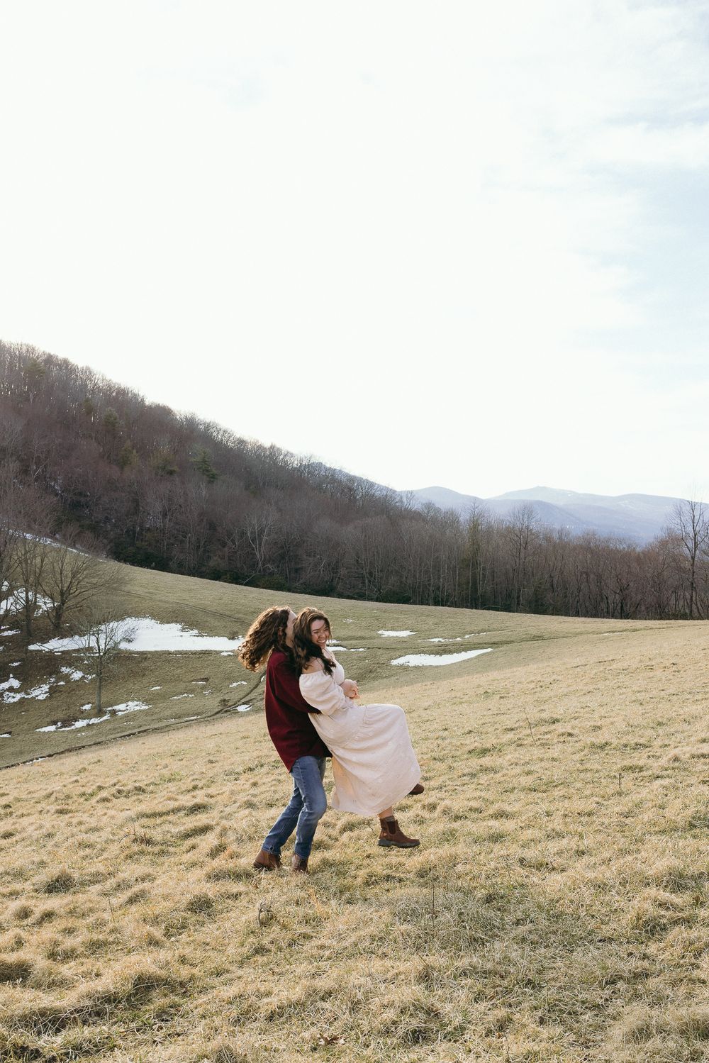 Two people dance and twirl in a grassy mountain meadow with patches of melting snow. Twickenham House Wedding Photographer