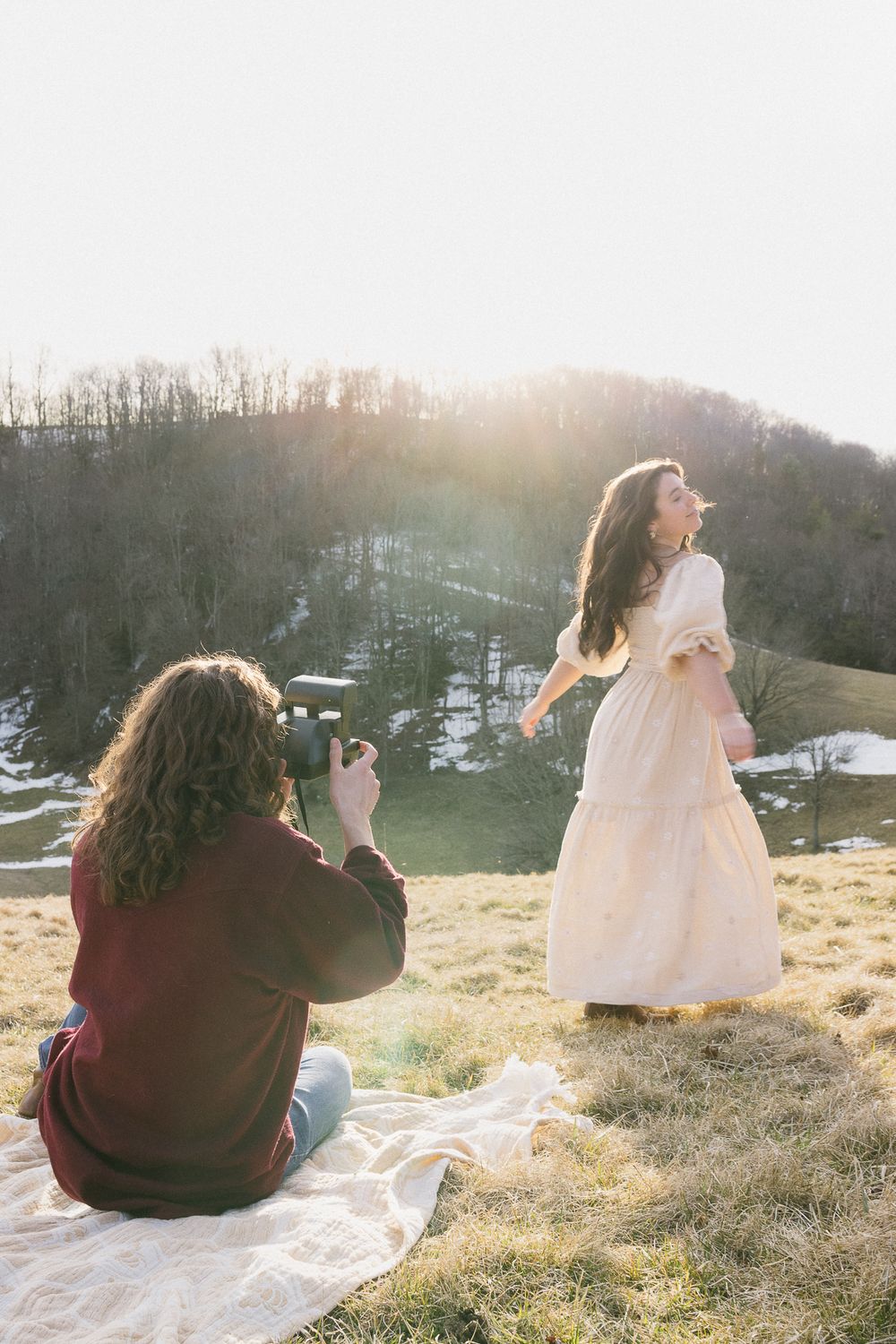 Two people sit on a blanket during a sunset photoshoot on a grassy hillside. Linbrook Heritage Estate Wedding Photographer