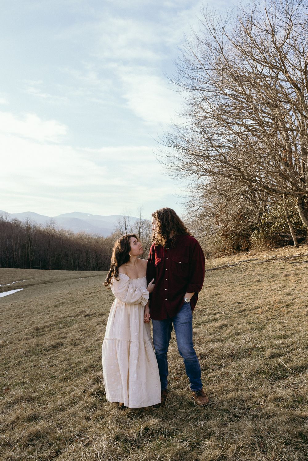 A couple stands together on a scenic hillside with bare trees and mountains in view. Twickenham House Wedding Photographer