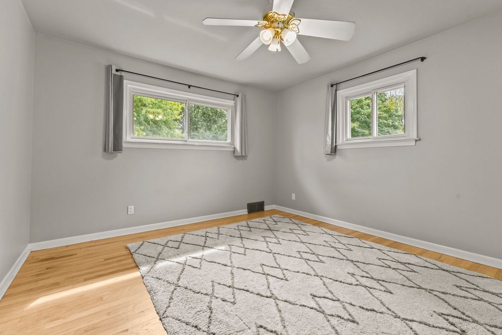 Spacious bedroom with hardwood floors, ceiling fan, geometric area rug, and two windows.