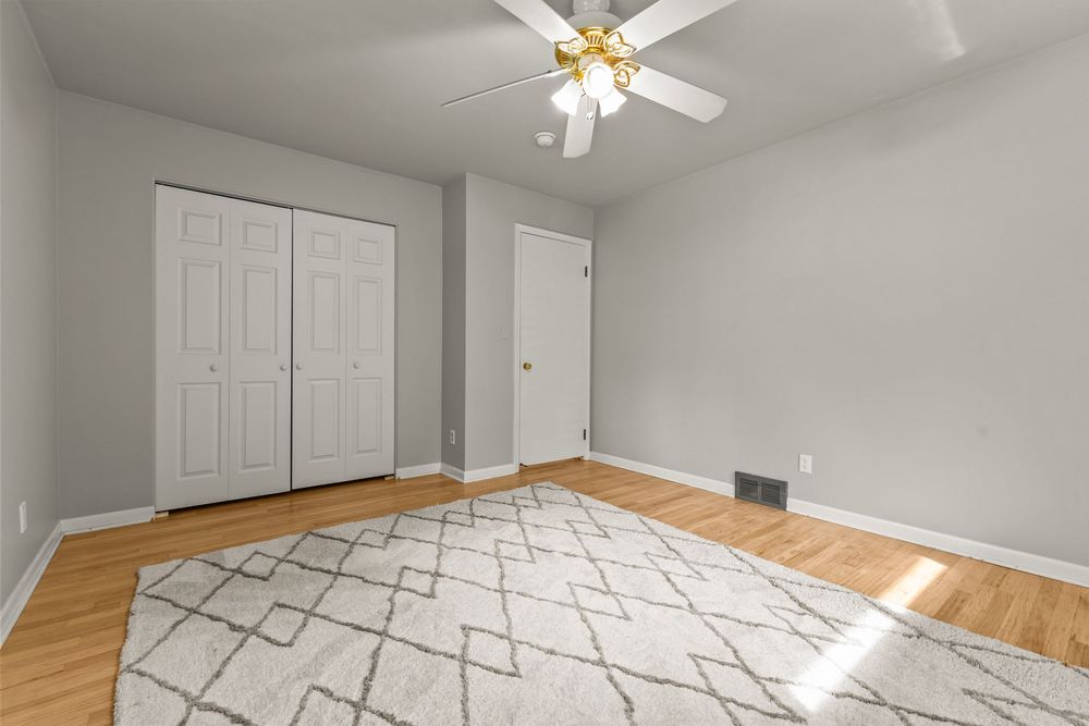 Bright bedroom with hardwood floors, white closet, ceiling fan, and geometric area rug.