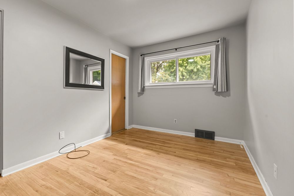 Minimalist bedroom with light hardwood floors, single window, and wall-mounted mirror.