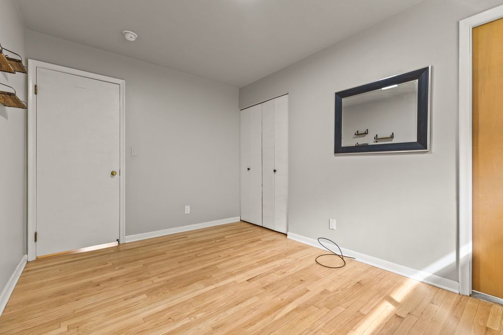 Empty bedroom with hardwood floors, two white closet doors, and wall-mounted mirror.