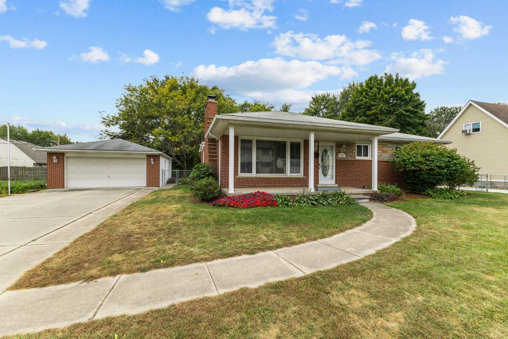 Brick ranch-style home with attached garage, manicured lawn, curved walkway, and mature trees.