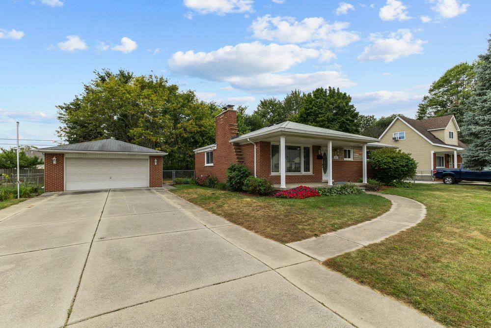Charming brick ranch home with detached garage, green lawn, and tree-lined street on a sunny day.