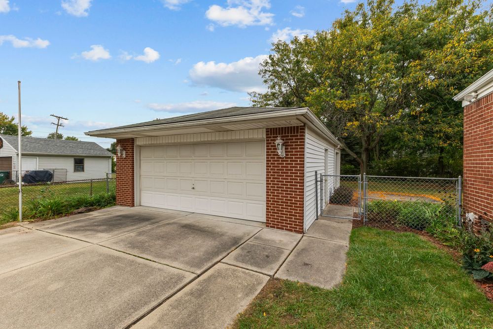 Detached brick garage with white double door, concrete driveway, and landscaped surroundings.