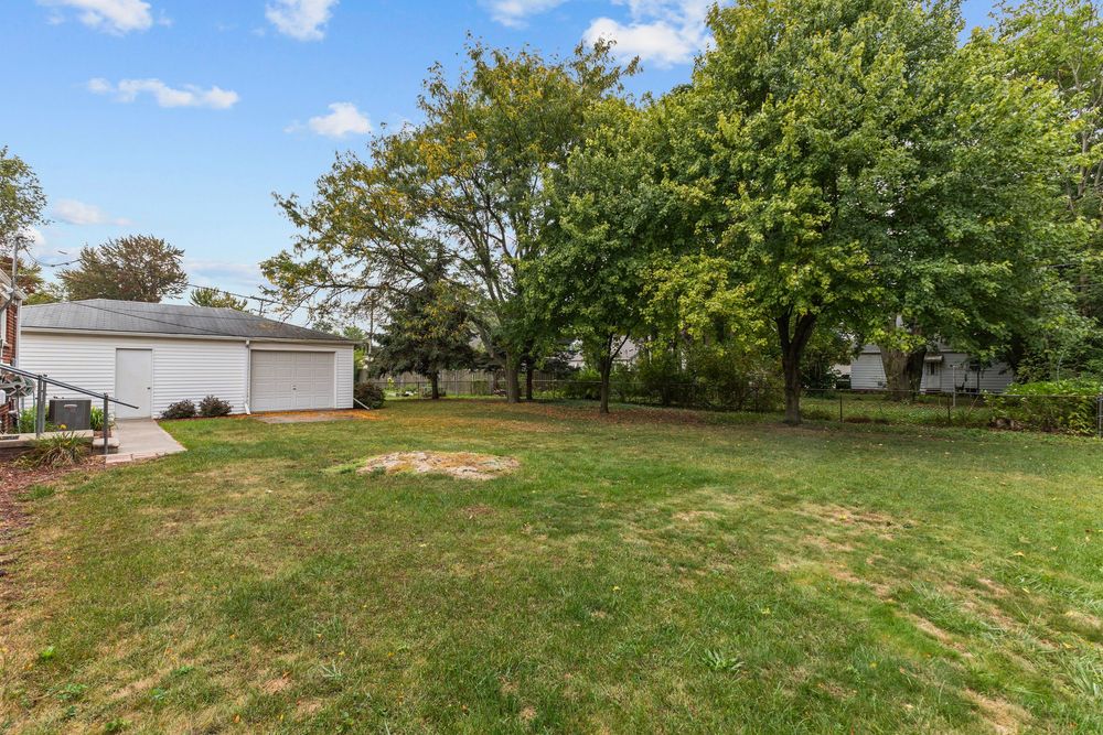 Expansive backyard with lush green lawn, mature trees, and detached garage visible in background.