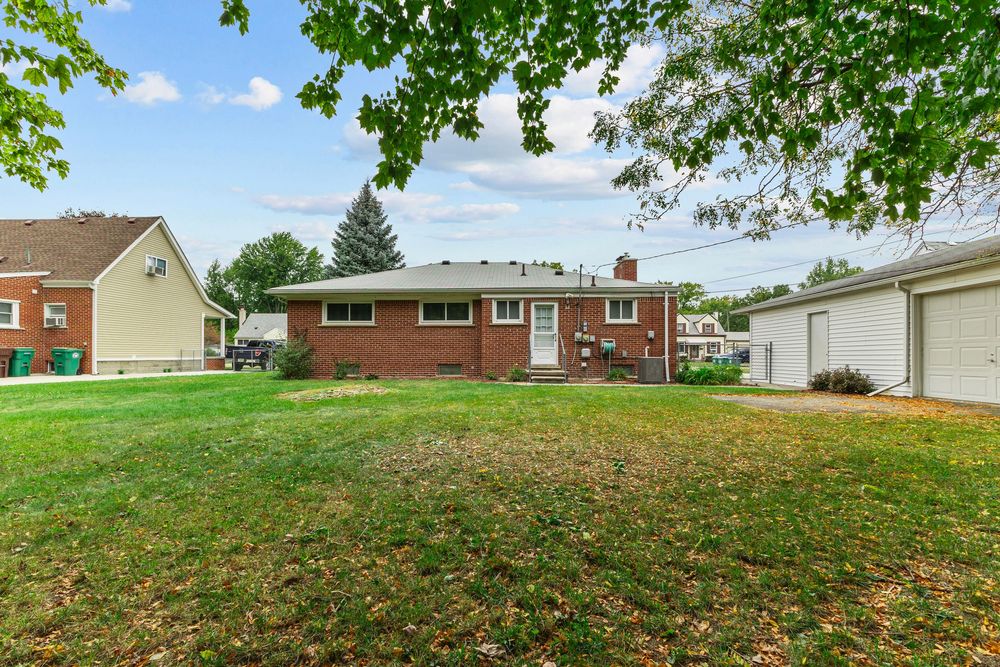 Brick ranch home with large green yard, detached garage, and mature trees on a clear day.