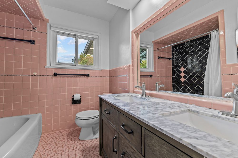 Pink-tiled bathroom with marble vanity, soaking tub, and decorative black shower tiles.