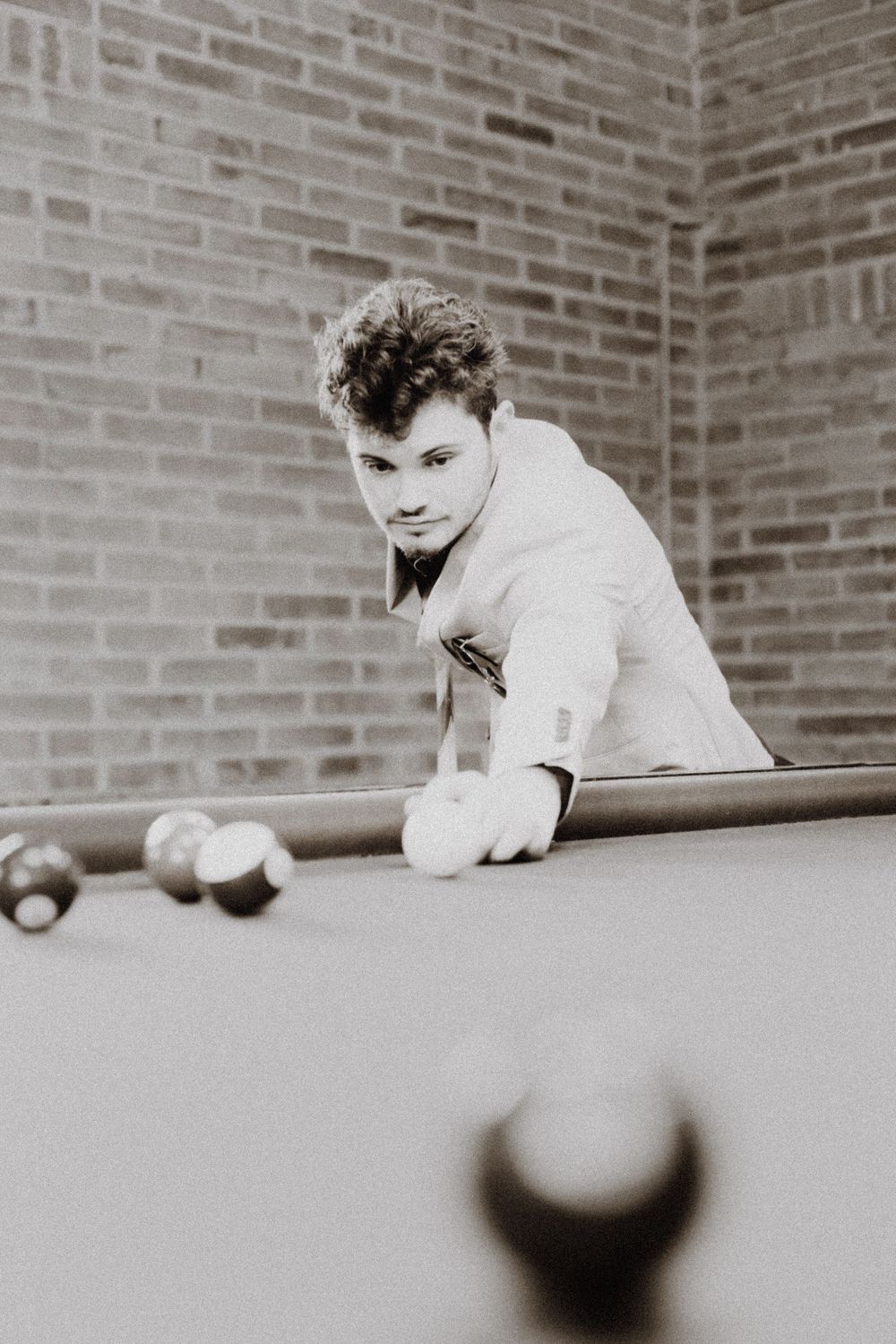 Black and white photo of person playing pool, leaning over table to line up shot.