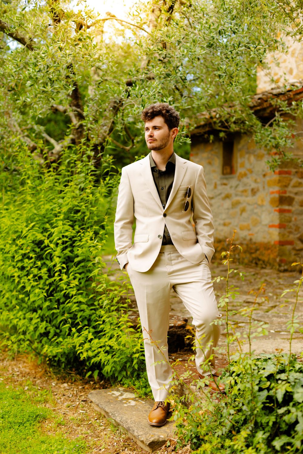 Person in light colored suit walks along garden path beside stone building.