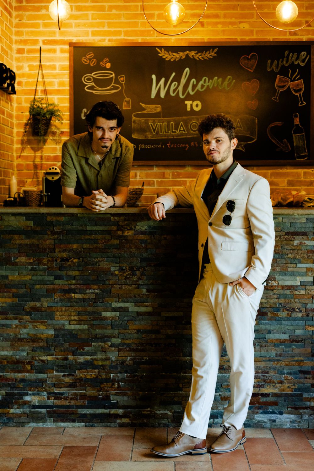 Interior of rustic cafe with exposed brick walls and welcome sign featuring two people at counter.