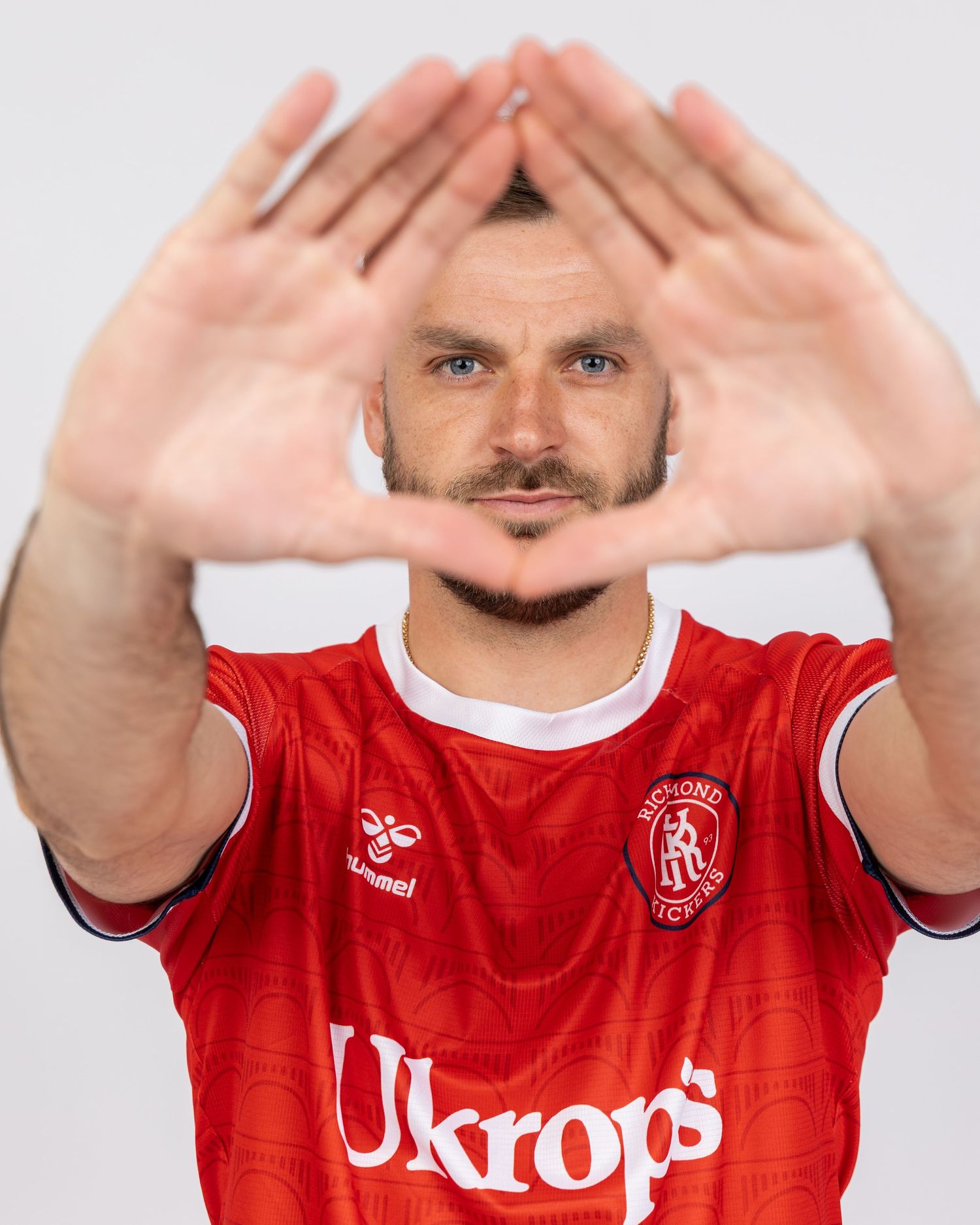 Person in red soccer jersey making heart shape gesture with hands against white background.