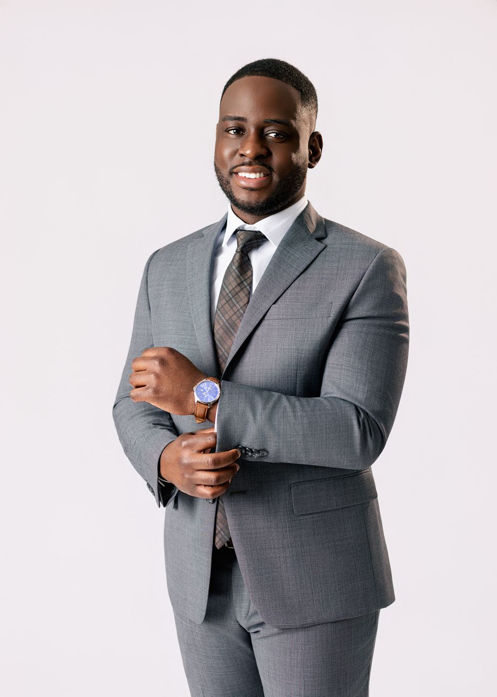 Professional portrait of someone in a well-fitted gray suit and tie standing against a white background.