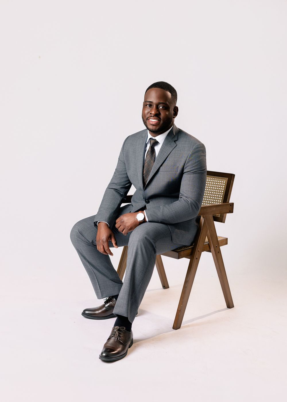 Professional portrait series showing a person in a well-fitted gray suit seated in a modern wooden chair against a white backdrop.