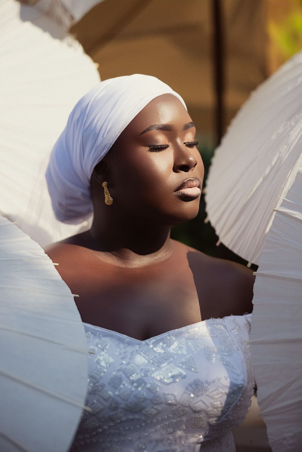 A bride in a white headpiece and wedding gown poses with closed eyes in an elegant artistic bridal portrait series.