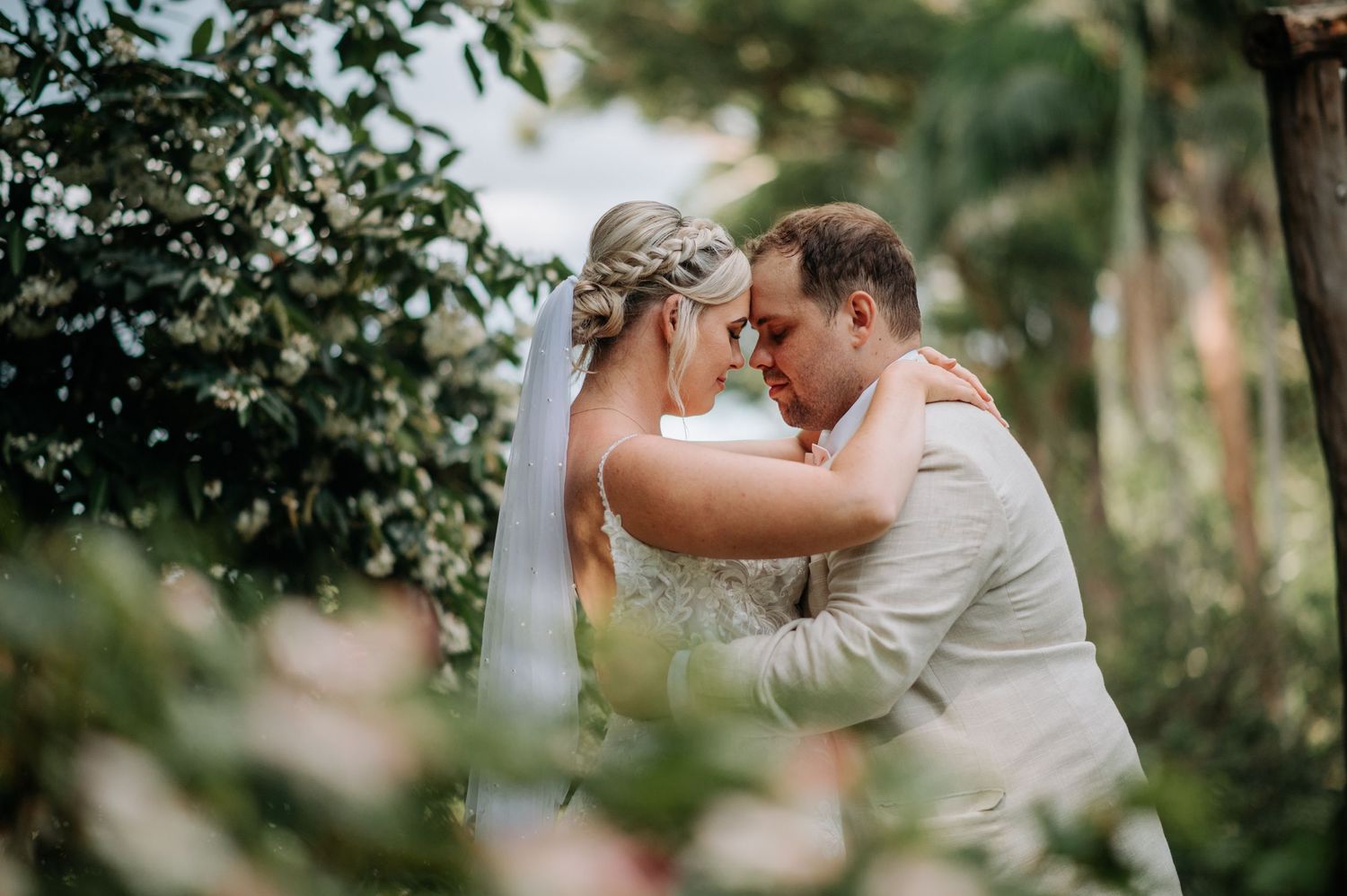 Intimate outdoor wedding moment captured among lush greenery and trees.