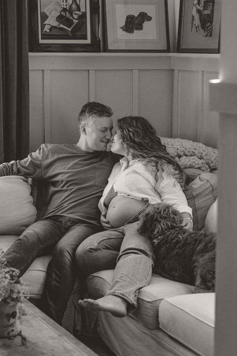 Black and white intimate moment between couple relaxing on couch with artwork visible above.