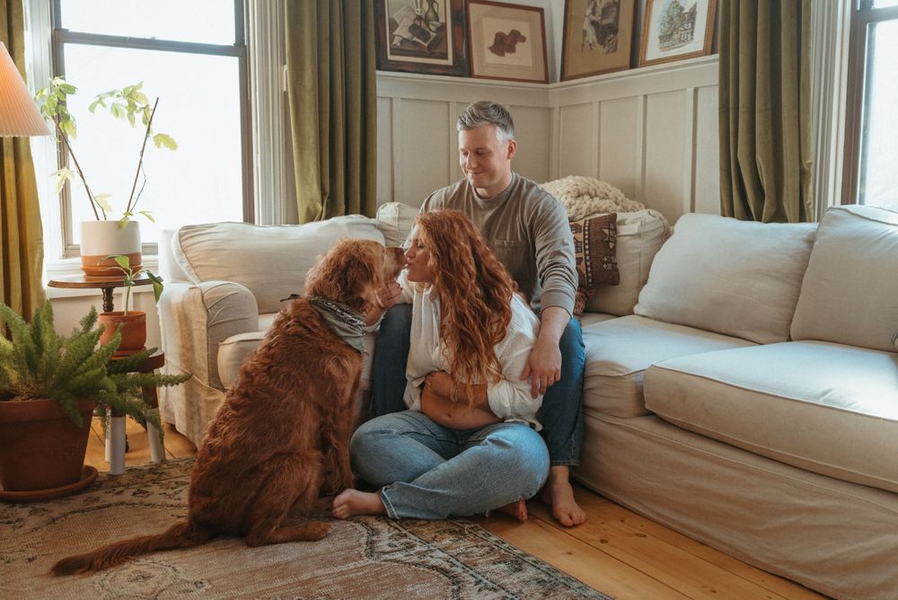 Couple sits on couch with brown dog in cozy living room setting.