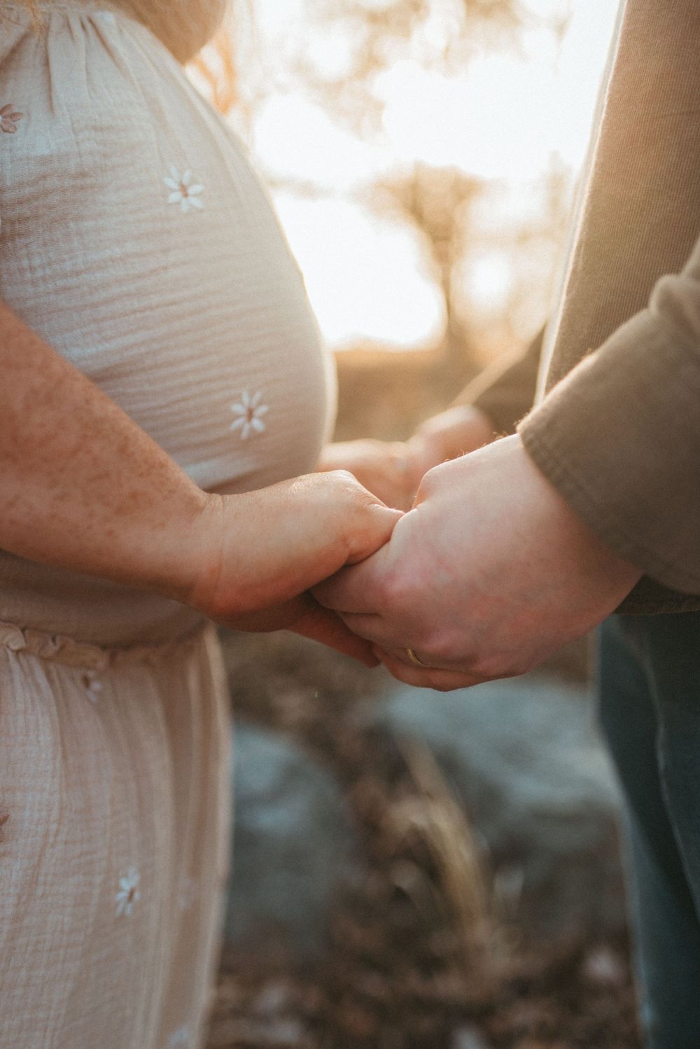 Couple holding hands in soft sunlight wearing white dress and casual attire while walking together.