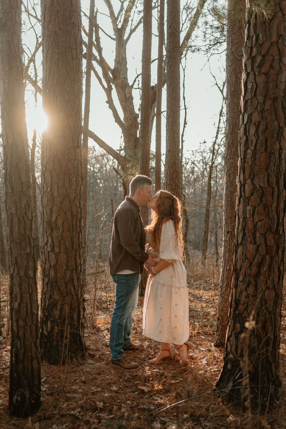 Intimate forest photoshoot with sunlight streaming through pine trees as couple poses together.