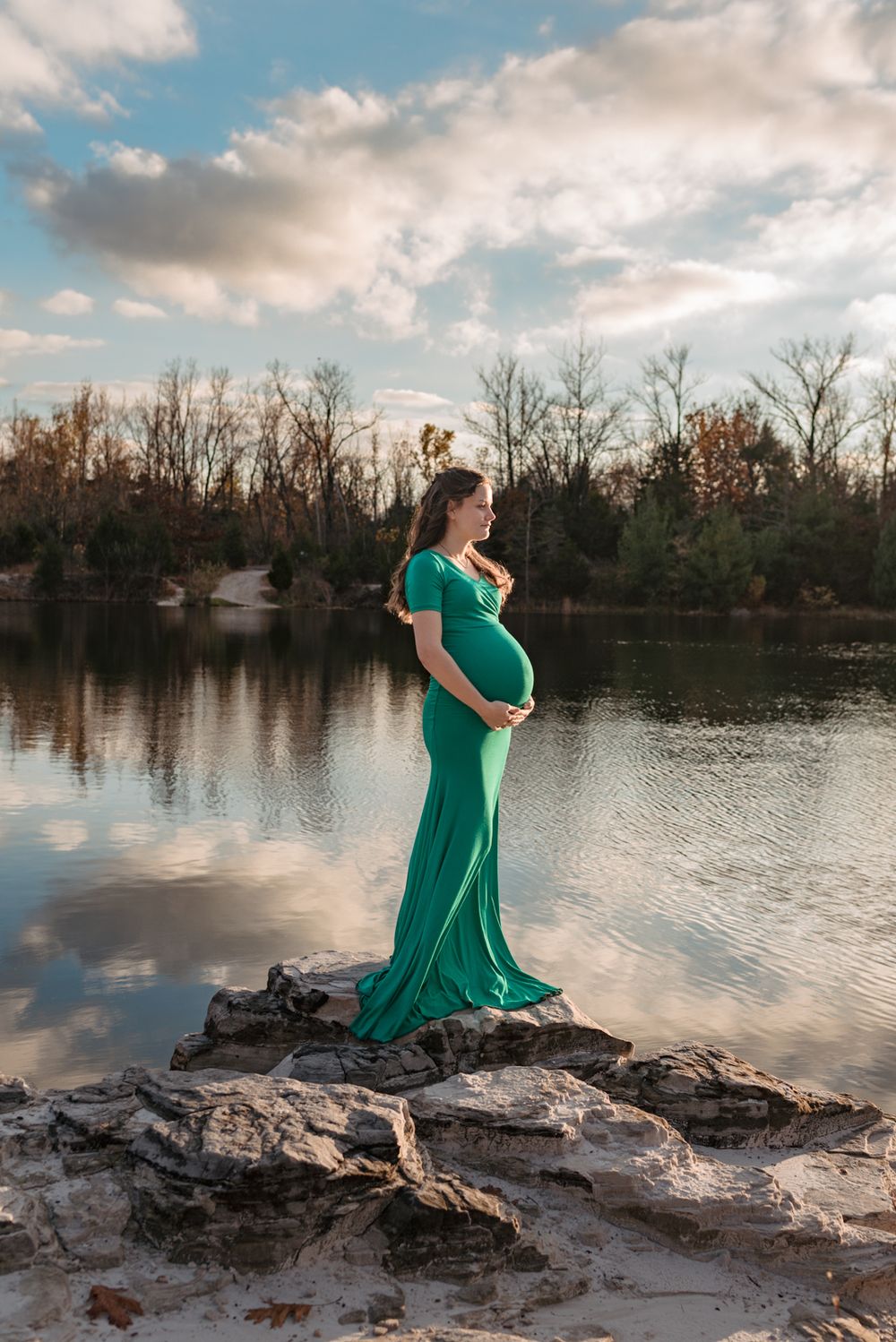 A maternity photo at sunset with a green dress against a reflective lake backdrop.