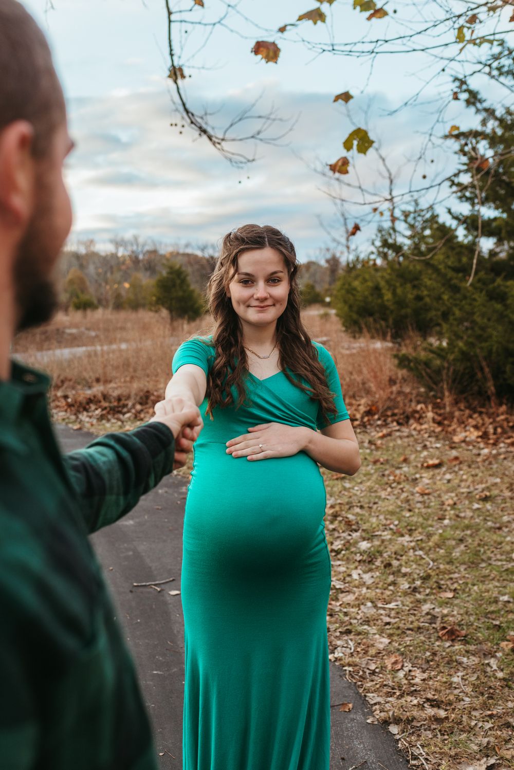 A sweet maternity moment captured on an autumn path with fallen leaves.