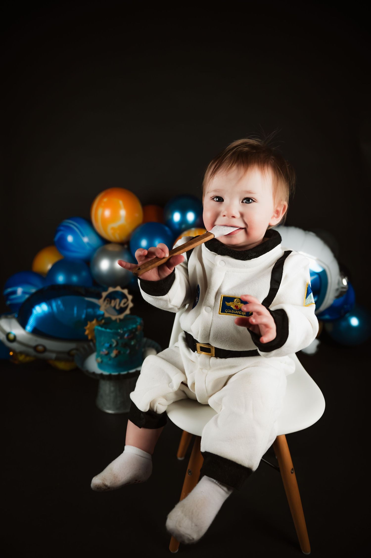 White party setup with balloons featuring small guest in white outfit sitting on wooden stool.