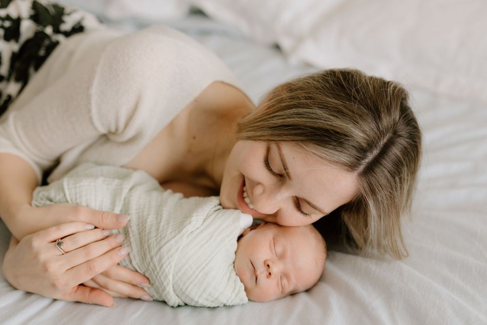 Tender moment between parent and sleeping baby on white sheets.