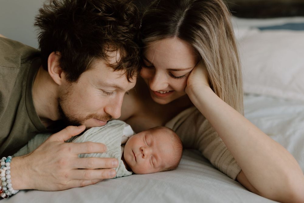 Loving family cuddle session with newborn on white bedding.
