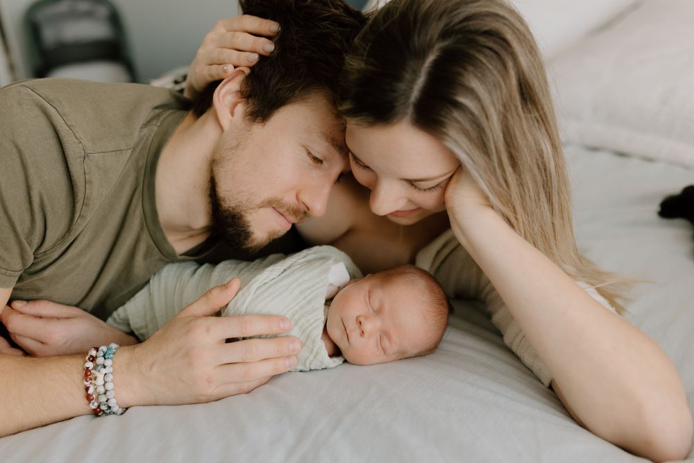 Parents sharing gentle moment with sleeping infant on bed.