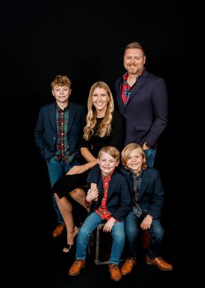 Studio portrait of a family of five in coordinating navy and red outfits against a black background.