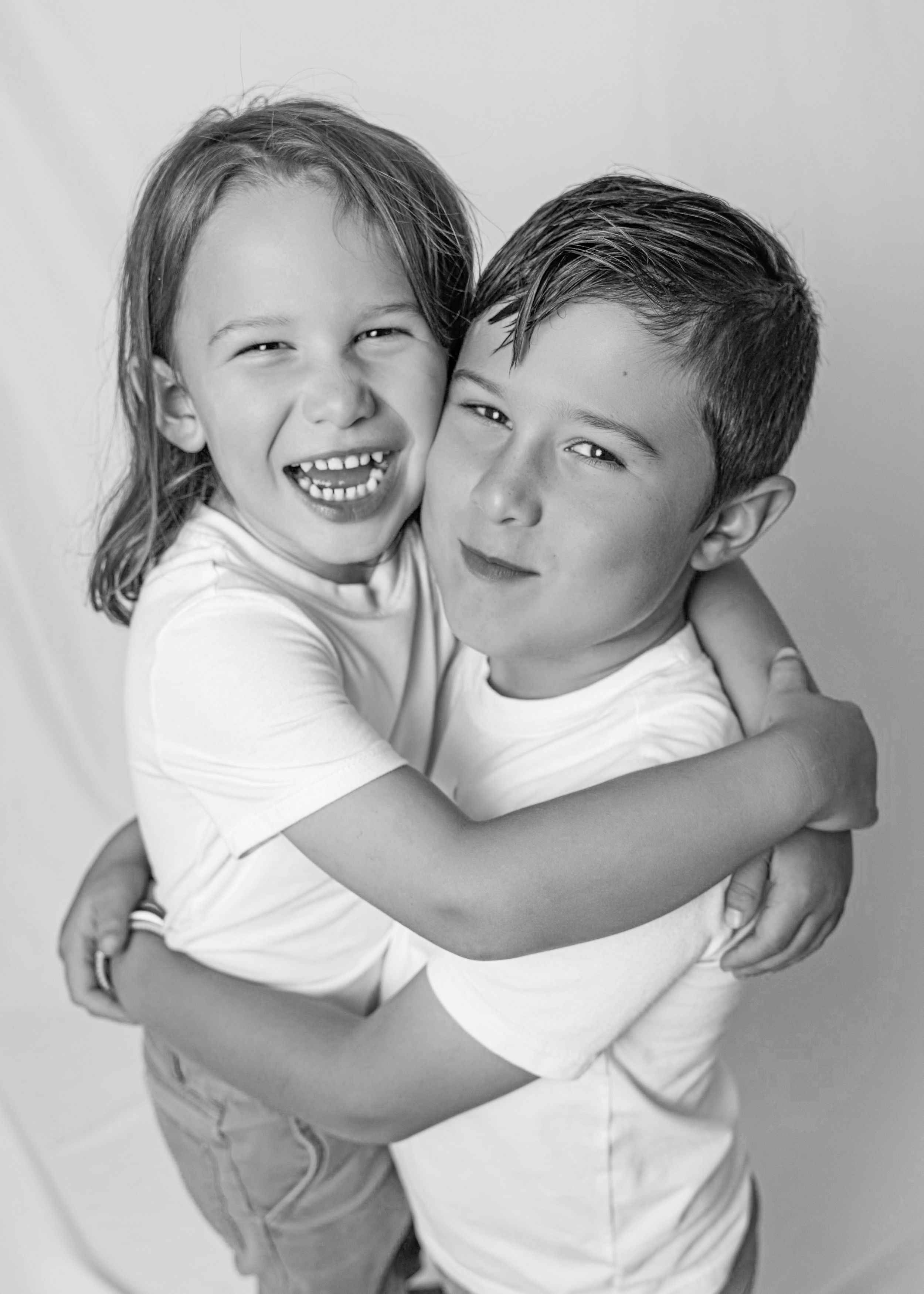 A heartwarming black and white portrait of two children embracing and showing playful expressions in white t-shirts.