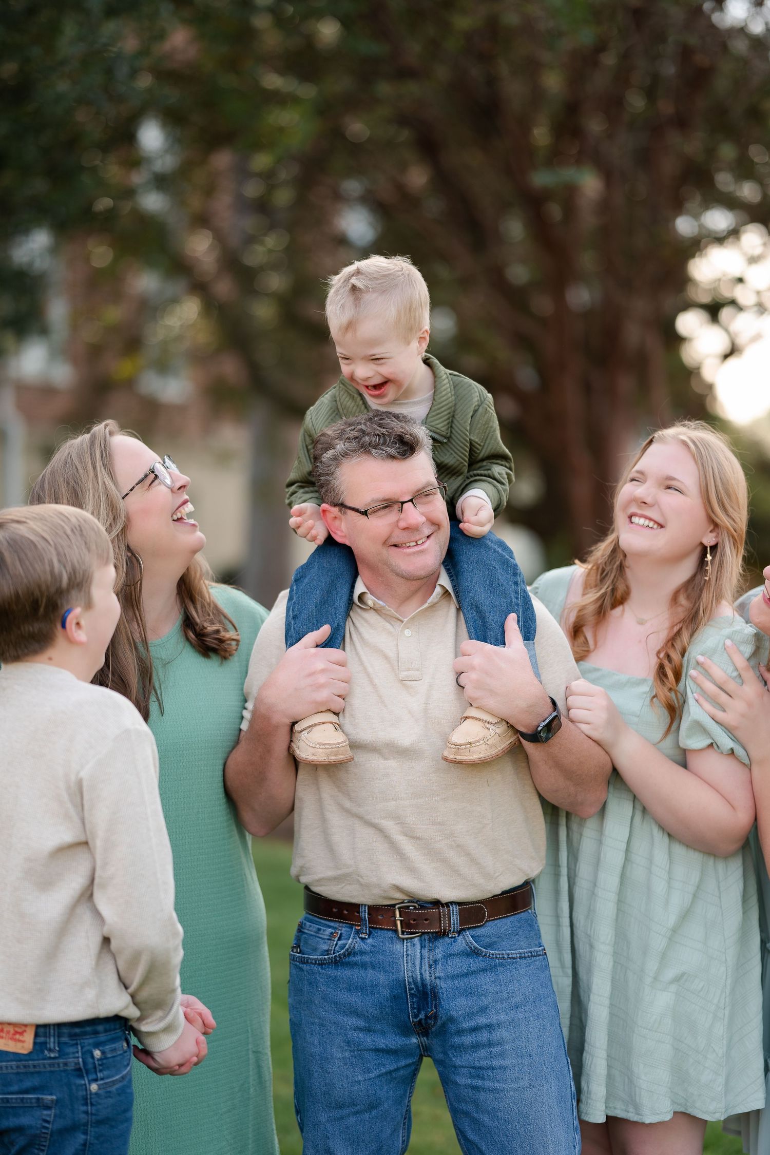 A joyful family portrait taken outdoors with coordinated casual outfits in neutral and mint green tones.