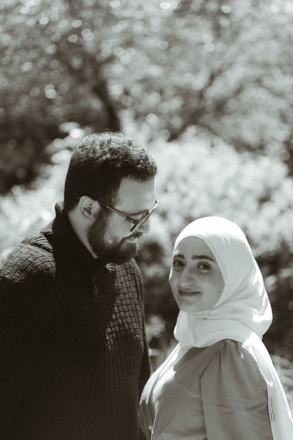 Black and white portrait of couple in outdoor setting with natural bokeh background.