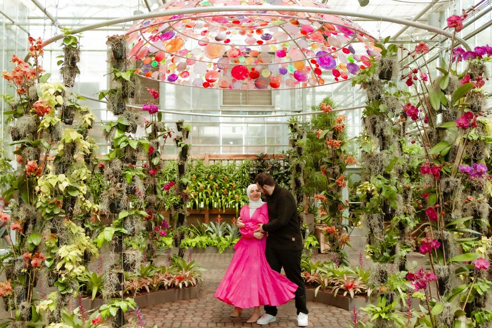 A couple dancing in a vibrant greenhouse filled with colorful orchids and hanging flowers.