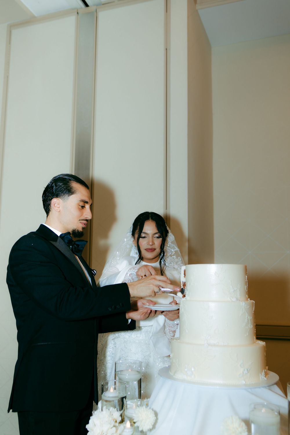 Wedding couple cutting their traditional white tiered cake together in formal celebration.