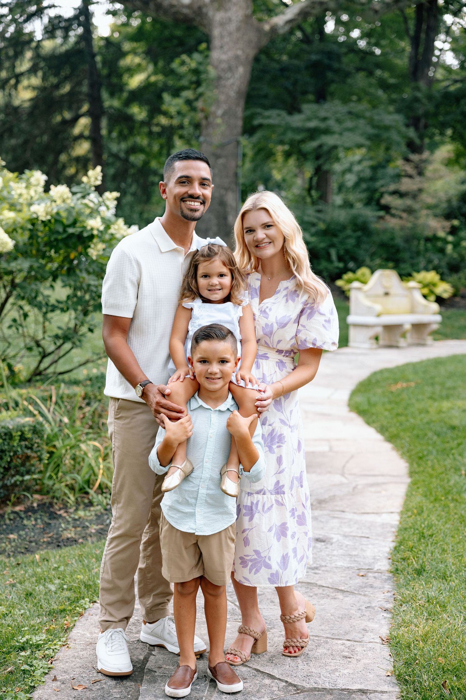 A beautiful family portrait in light summer clothing against blooming hydrangea bushes and white gazebo.