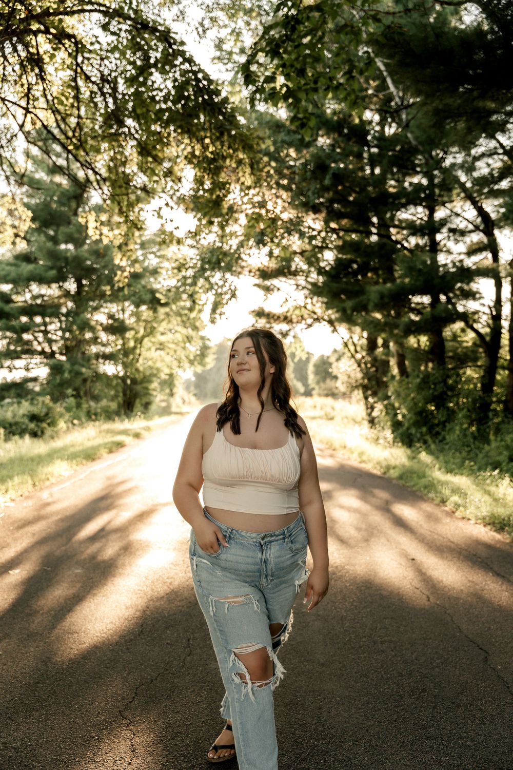 Casual summer photoshoot on a sunlit path wearing distressed denim and white top.
