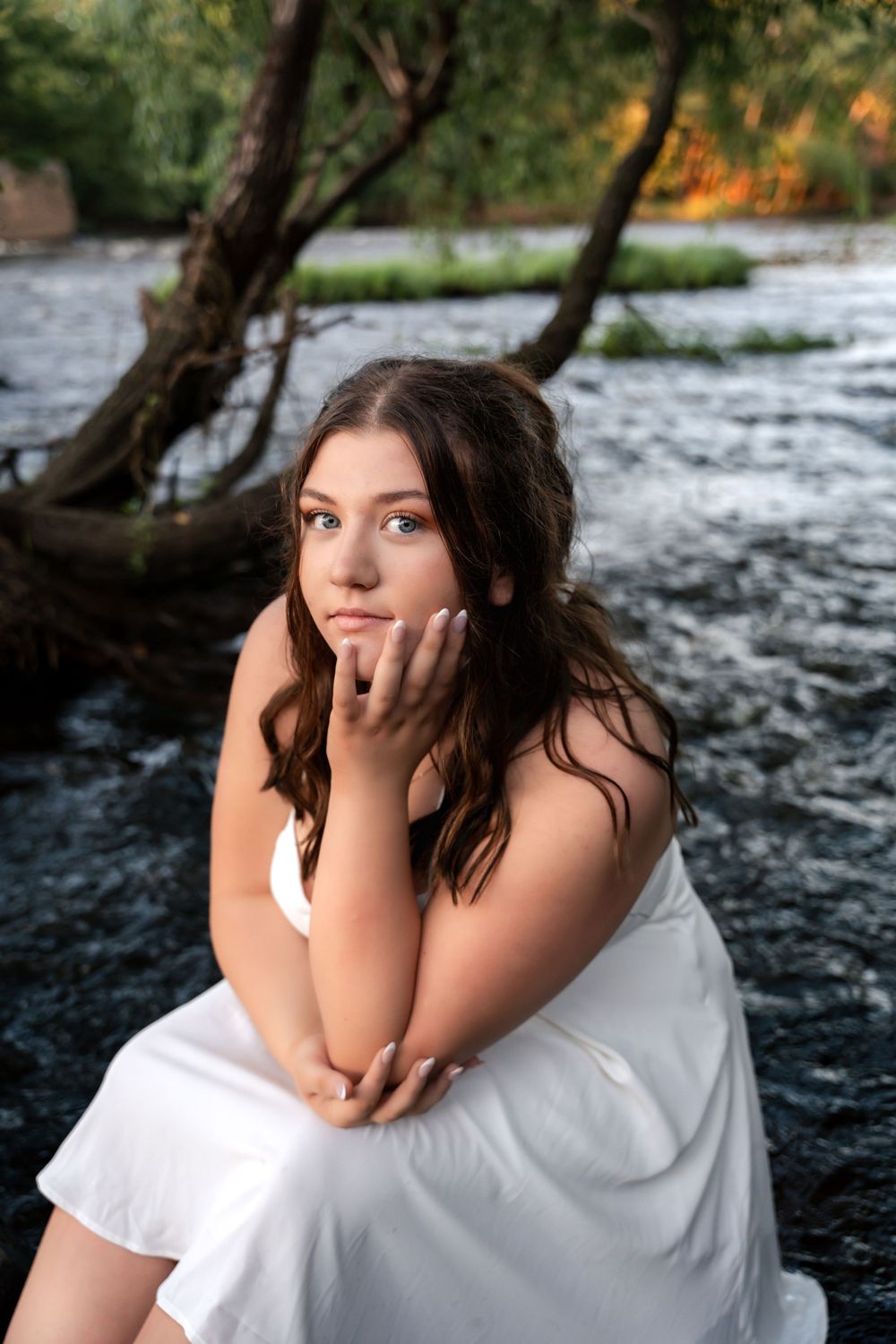Dreamy portrait session near flowing water with white fabric and natural elements.