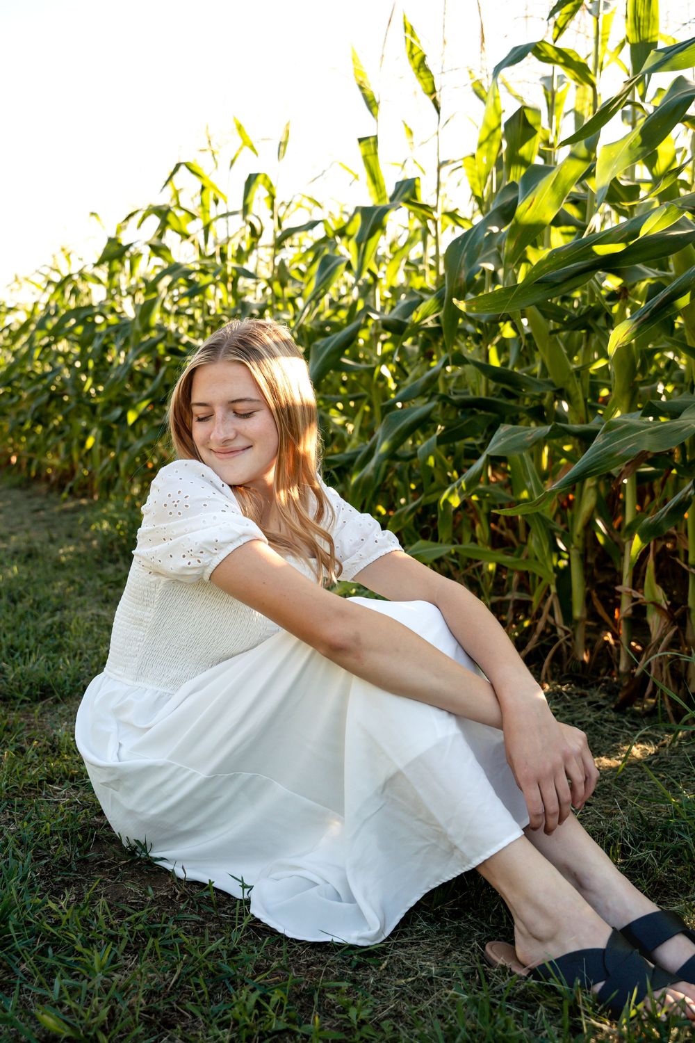 A person in a white dress relaxes by a cornfield on a sunny day.