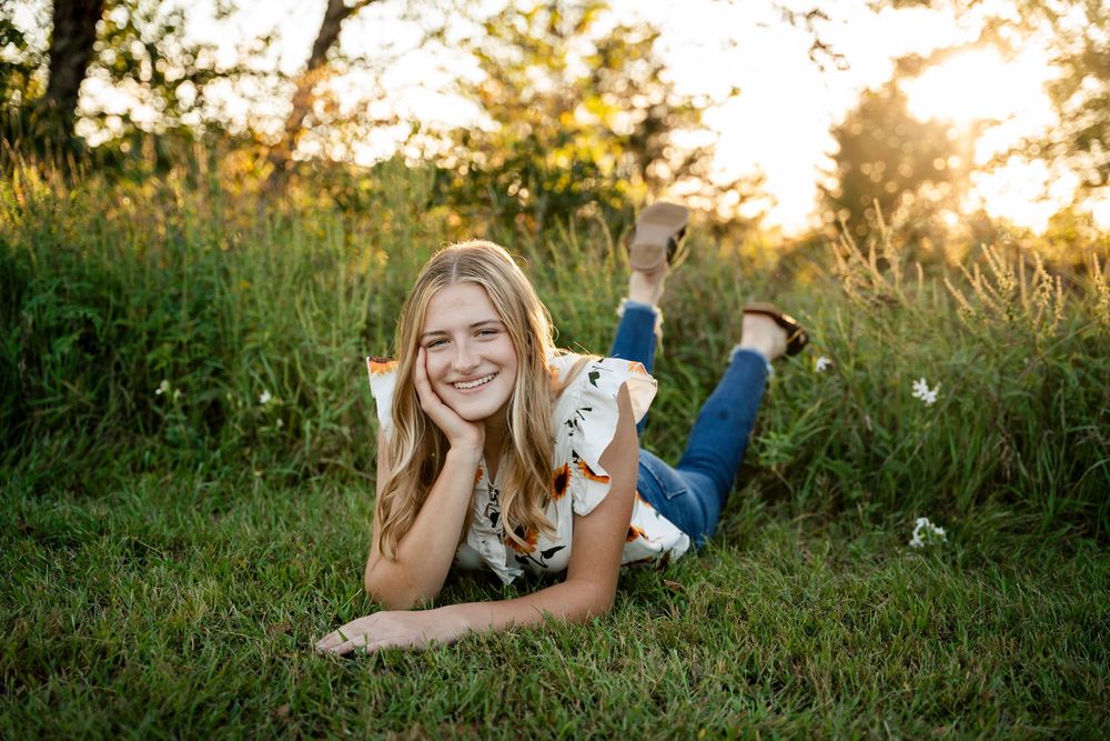 A person poses in a sunlit field wearing a floral top during sunset.