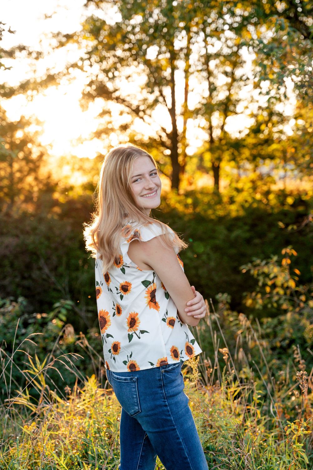 A person in a floral top laughs while posing in golden evening light.