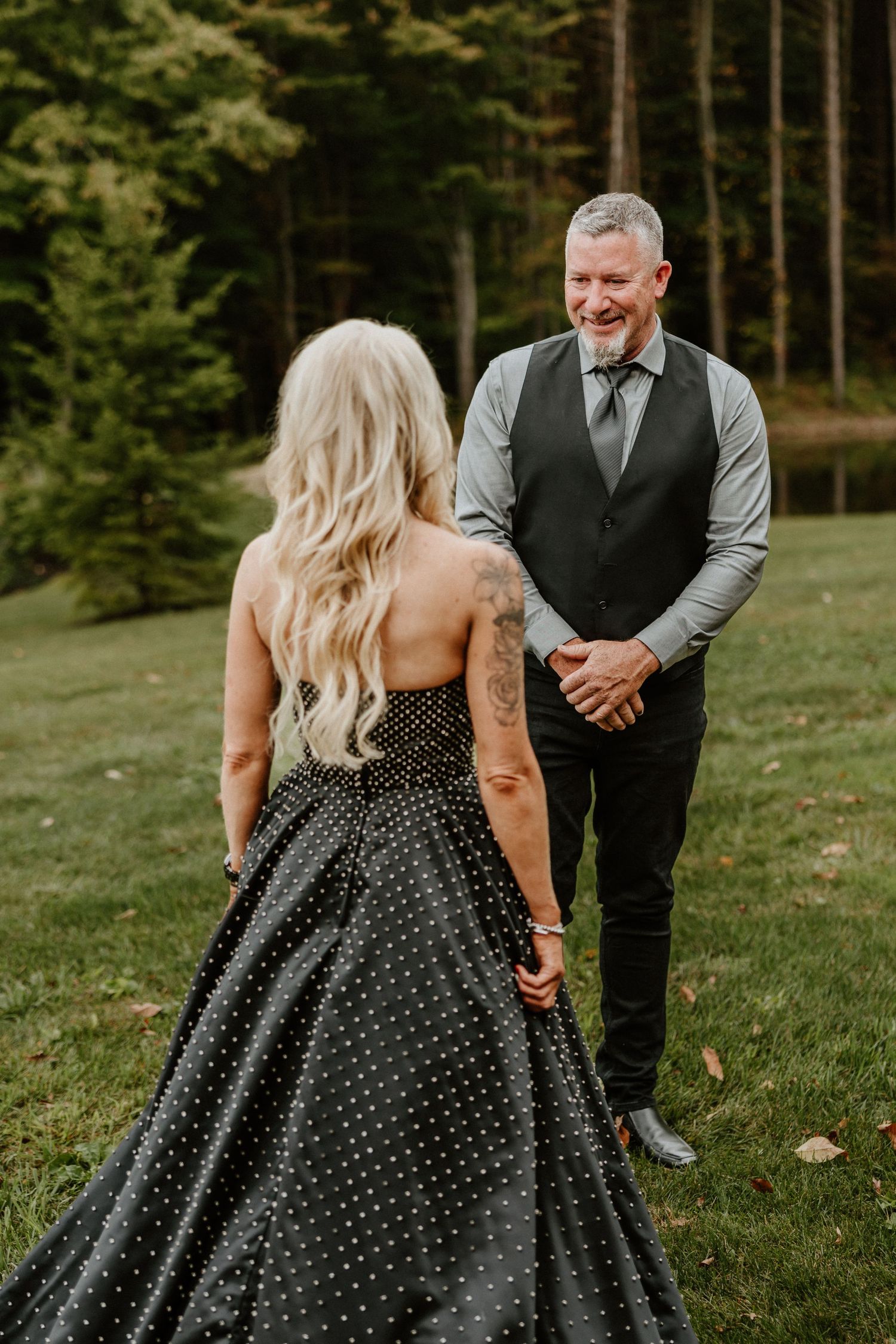 Couple in formal attire sharing intimate moment outdoors with forest backdrop.