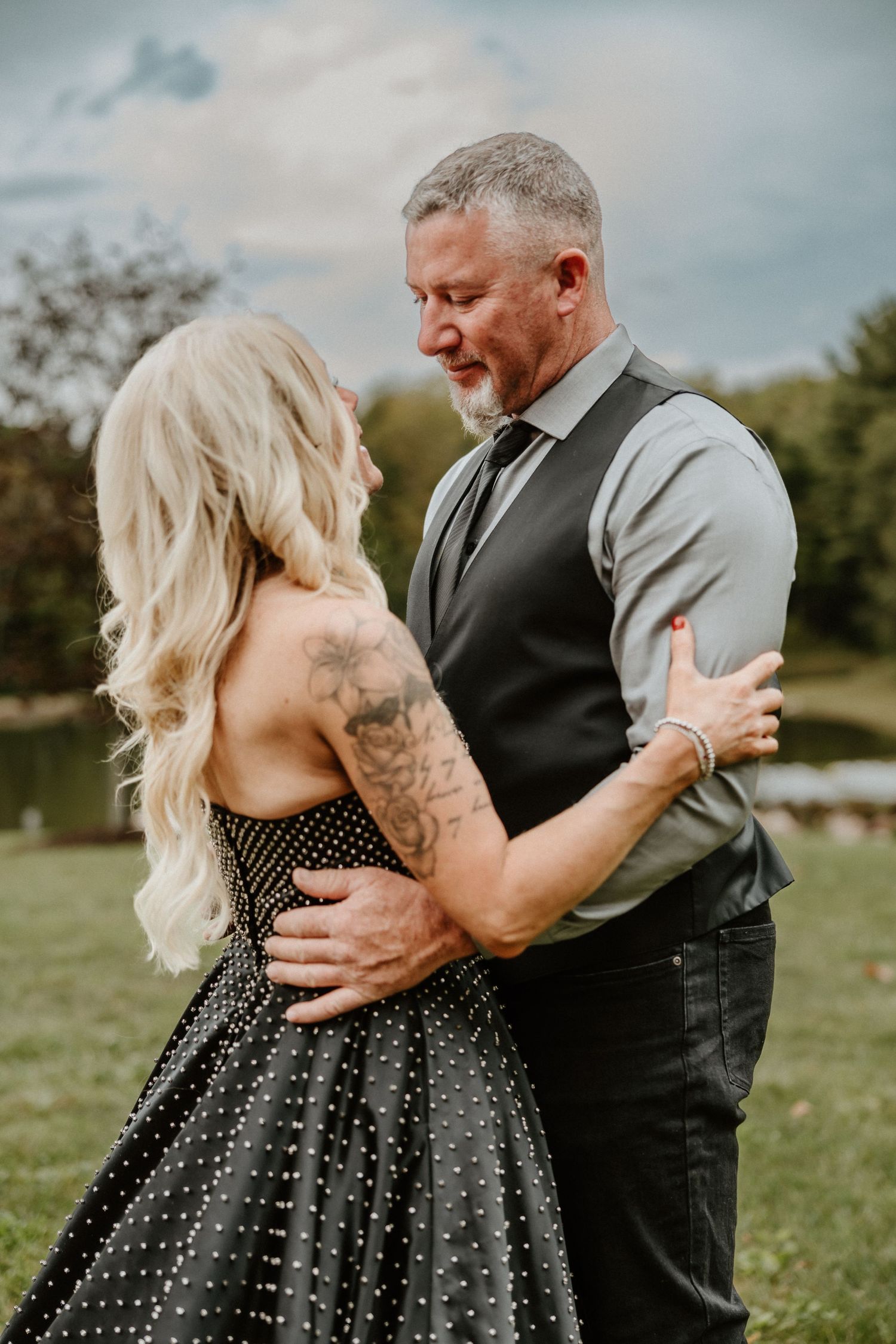 Intimate embrace between couple in formal wear on grassy hillside.