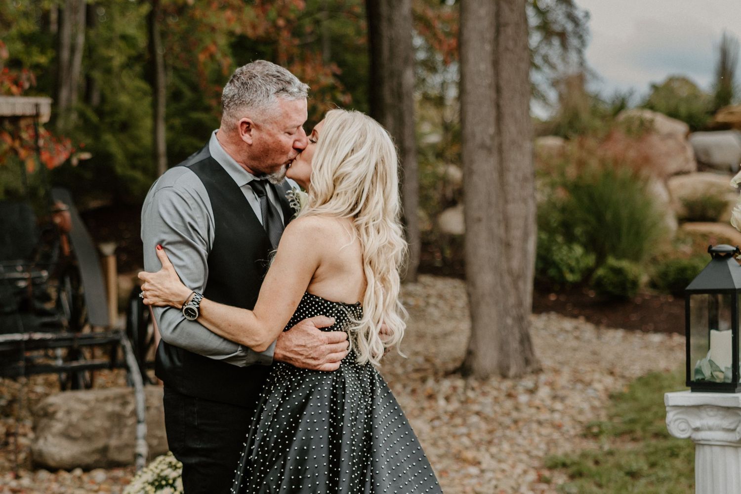 A tender embrace between newlyweds in an outdoor garden setting with stone features.