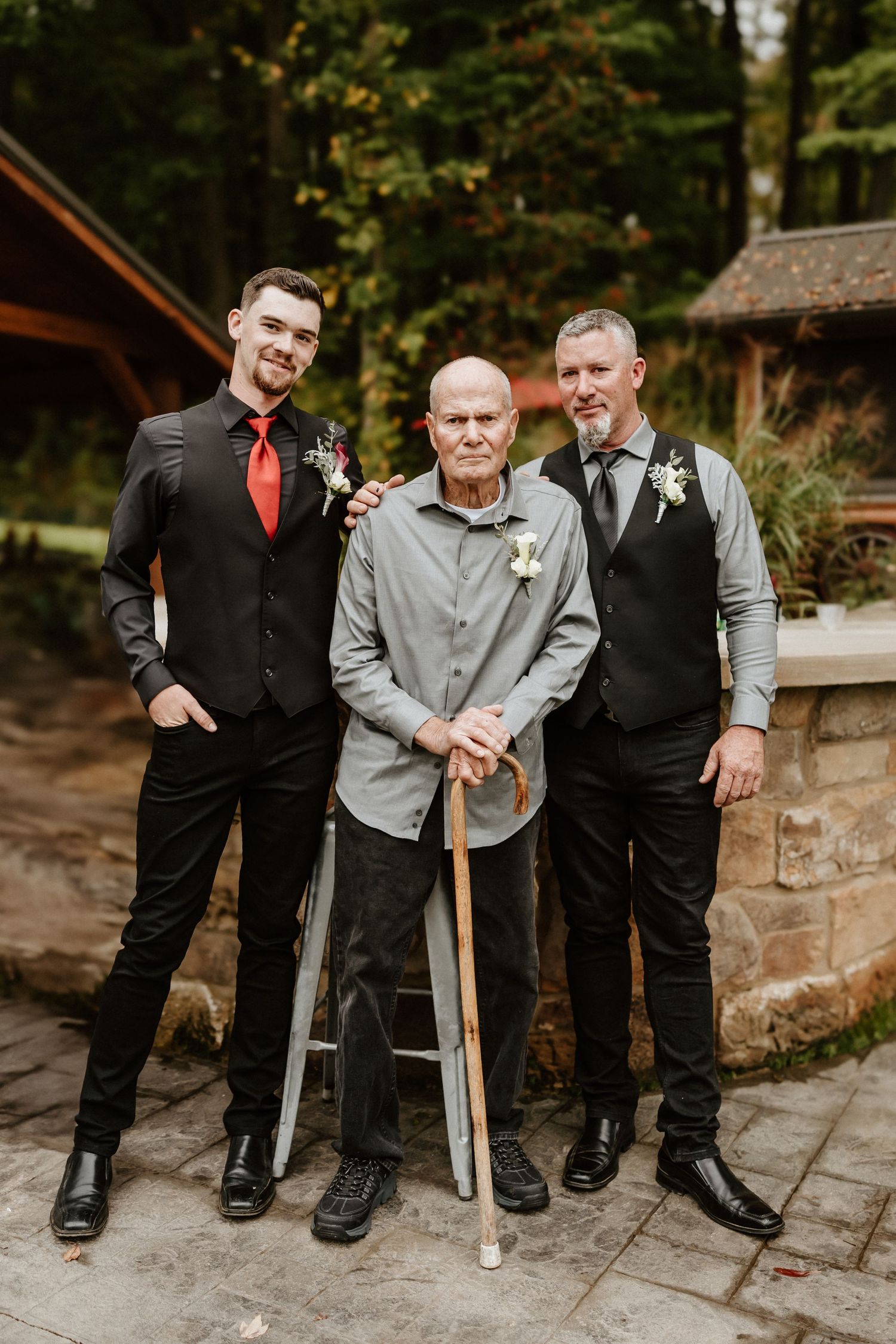 Three people pose together on stone patio with rustic cabin in background.