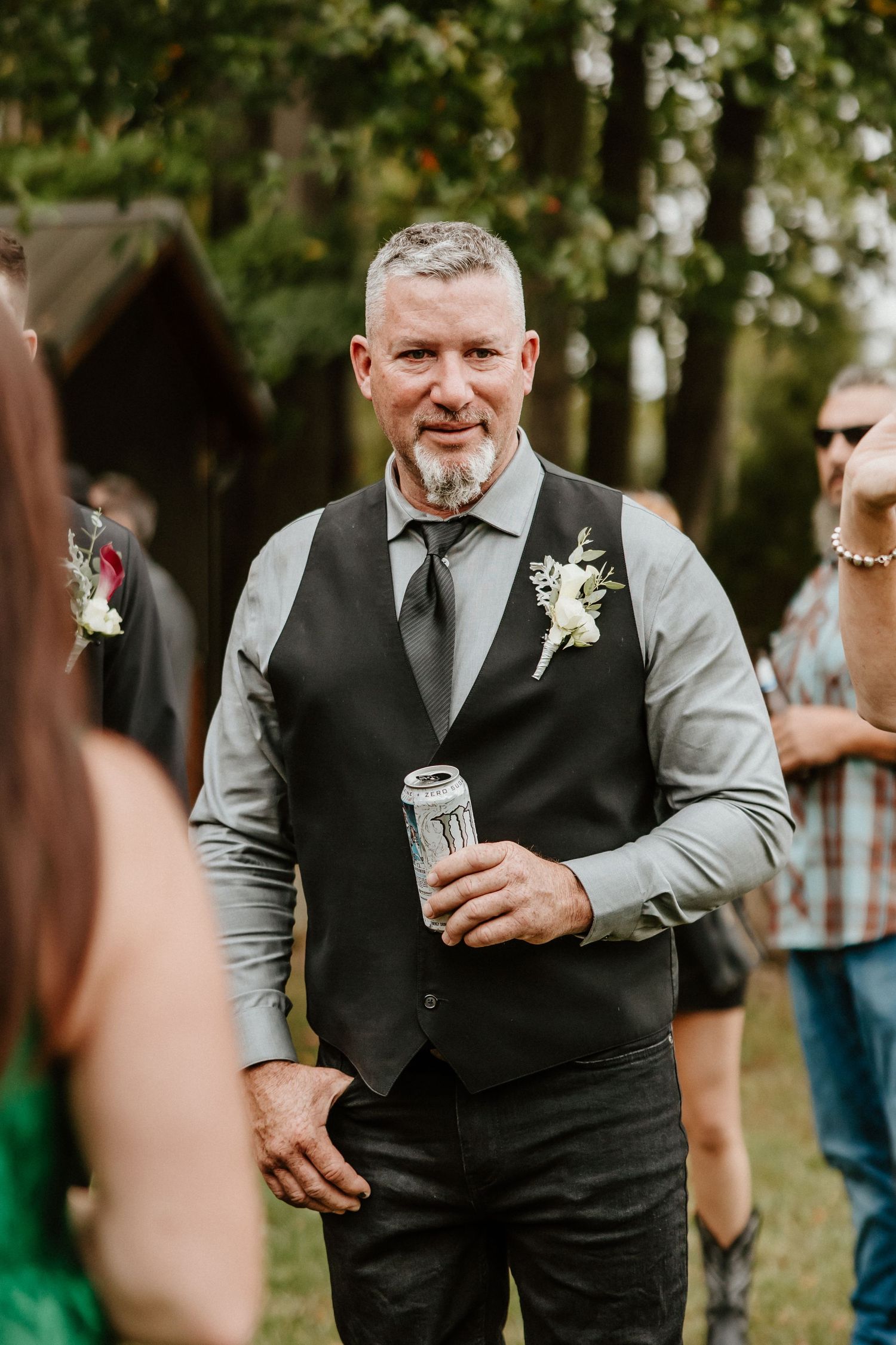 Person in formal attire holding beverage during outdoor wedding reception.